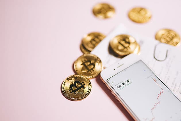 Pink flat lay with phone showing cryptocurrency stocks and scattered bitcoin