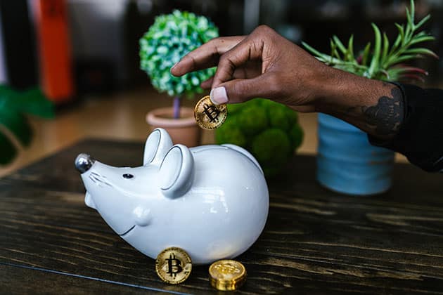 Image of tattooed man putting bitcoins into a mouse-shaped piggy bank