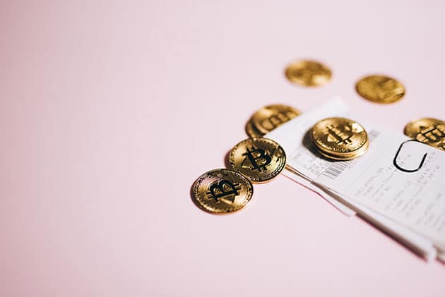 Picture of bitcoin on top of a stack of receipts against a pink background