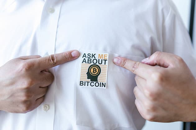 Picture of man in white button up shirt with pin that says ask me about bitcoin