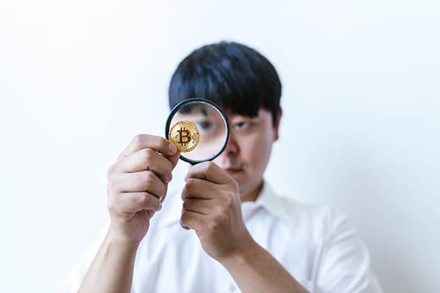 man holding magnifying glass inspecting a bitcoin