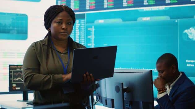 Business analyst holding a laptop in front of a digital screen of financial information